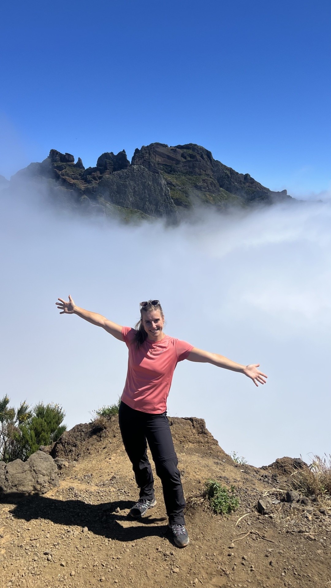Katharina steht mit ausgebreiteten Armen auf einem Berggipfel über dem Wolkenmeer – Sinnbild für Freiheit und Selbstvertrauen beim Solo-Reisen